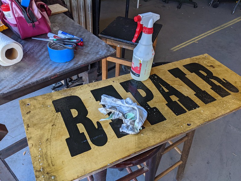 a wooden sign painted with the word REPAIR in an old fashioned font, on a workbench