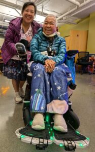 Two asian american women smiling, one seated in powerchair with lights attached