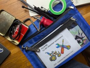 a colorful zine and some tools coming out of a zippered pencil pouch