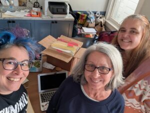 liz, karen, and veronica smiling in front of a box of papers, a scanner, and laptop